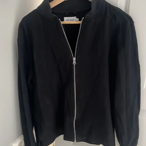 Svart helzip från East West - Säljer en stilren svart helzip från East West med dragkedja framtill. Tröjan passar perfekt nu till våren och kan användas såväl dagligen som vid finare tillfällen 