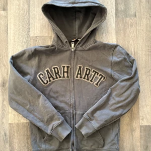 Grå Carhartt hoodie - Säljer en grå Carhartt hoodie med dragkedja och nice logga på framsidan.
