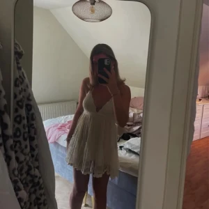 Vit klänning med spetsdetaljer - Charmig vit klänning med spetsdetaljer och volanger. Klänningen är axelbandslös och har en öppen rygg med knytband. Perfekt för sommarens festligheter. 