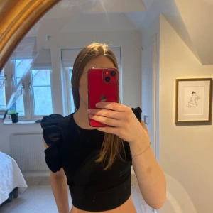 Svart kortärmad topp med volangdetalj - Säljer en stilren svart topp med korta ärmar och en elegant volangdetalj på axeln. Storlek S