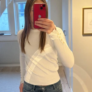 Vit långärmad tröja med knappar - Säljer en stilren vit långärmad tröja med dekorativa knappar på ärmarna. Tror det är storlek s men är inte säker så lappen inte fina kvar