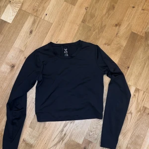 Svart träninglångärmad topp från SOC - Säljer en svart långärmad topp från SOC i storlek XS. Toppen har en stilren design med vita detaljer på baksidan och är tillverkad i ett tekniskt material som andas. Perfekt för träning eller en aktiv vardag.