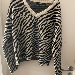 Zebramönstrad tröja från Vero Moda - Säljer en snygg zebramönstrad tröja från Vero Moda. Tröjan har en v-ringad hals och långa ärmar, perfekt för att sticka ut i mängden. Den är i svart och vit med en ribbad kant vid halsen.