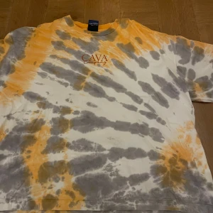 Tie-dye t-shirt från Cava Company oversized - Säljer en cool tie-dye t-shirt från Cava Company i orange och grått. T-shirten har ett tryck med märkesnamnet på bröstet och är kortärmad. Perfekt för en avslappnad stil.