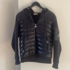 Svart jacka från Moncler - Snygg svart jacka från Moncler med quiltad design och dragkedja. Jackan har långa ärmar och en huva med dragsko. Perfekt för kyligare dagar med stil.10/10 skick äkta såklart‼️