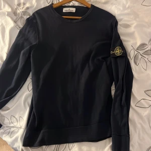 Svart långärmad tröja från Stone Island - Säljer en stilren svart långärmad tröja från Stone Island. Tröjan har en rund halsringning och det ikoniska Stone Island-märket på ärmen. Perfekt för en avslappnad och trendig look.