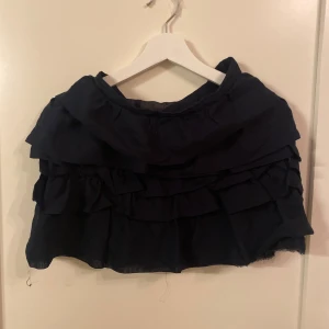 Svart volangkjol från H&M - Snygg svart kortkjol från H&M med flera lager av volanger som ger en lekfull look. Perfekt för att addera lite extra stil till din outfit. Tillverkad i ett lätt och bekvämt material.