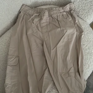 Cargo Byxor - Beige cargo byxor med fickor på sidan.