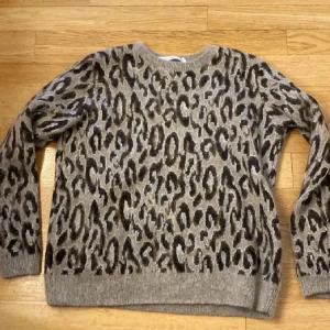 Leopardmönstrad tröja från & Other Stories - Säljer en snygg leopardmönstrad tröja från & Other Stories. Tröjan har en grå bas med svarta och bruna fläckar, perfekt för att sticka ut i mängden. Den är långärmad och har en rund halsringning. Perfekt för höst och vinter! 
