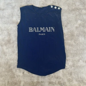 Mörkblå ärmlös topp från Balmain - Snygg mörkblå ärmlös topp från Balmain med tryck på framsidan. Perfekt för en stilren och avslappnad look. Tillverkad i mjukt material för extra komfort. Väldigt bra skick. Bara använd ett fåtal gånger. Storlek 38/S