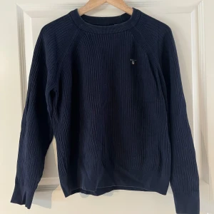 Mörkblå stickad tröja från GANT - Säljer en stilren mörkblå ribbad tröja från GANT. Tröjan har en klassisk design med rund hals och långa ärmar. Kontakta ifall frågor 