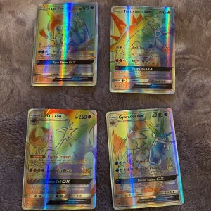 Pokémon GX-kort - Säljer fyra Pokémon GX-kort: Tapu Fini GX, Turtonator GX, Lunala GX och Gyarados GX. Dessa kort har en holografisk yta och är perfekta för samlare eller spelare som vill förstärka sin kortlek. Kortens baksida har den klassiska Pokémon-designen med en Pokéball.