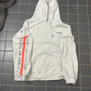 Vit hoodie från FB Sister - Säljer en vit over sized hoodie från FB Sister med texten 'MOOD' på bröstet och 'NOT MY PROB' längs ärmen. Hoodien har en orange rand som detalj och en klassisk känguruficka framtill. Perfekt för en avslappnad stil.