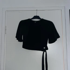 Svart omlottopp - Svart ”ballerina” liknande topp med urringning och volangärmar. Långa snören, så passar även bra att göra en rosett. 💝