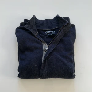 Mörkblå tröja med dragkedja och knapar från Massimo Dutti - Säljer en stilren mörkblå tröja från Massimo Dutti i bomull och kashmir. Tröjan har en dragkedja framtill och ribbade detaljer vid kragen. Perfekt för en elegant och avslappnad look.