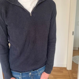 Dressman half zip - Säljer en stilren mörkgrå stickad tröja med dragkedja vid halsen. Perfekt för kyligare dagar med sin ribbade struktur och långa ärmar. En klassisk och bekväm tröja som passar till det mesta.