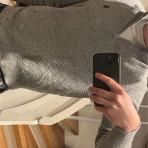 Grå tröja från Polo Ralph Lauren - Säljer en stilren grå tröja från Polo Ralph Lauren med dragkedja vid halsen. Tröjan har ett diskret märke på bröstet och är tillverkad i ett mjukt material. Perfekt för en avslappnad look.