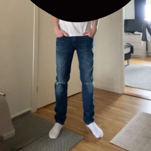 Replay jeans med slitningar - Snygga blå jeans med slitningar på knäna och låren. De har en klassisk femficksdesign och en dragkedja. Perfekta för en avslappnad stil. Modell: Kelligray W27L32 