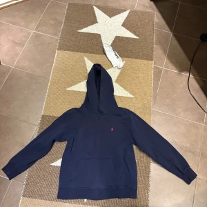 Polo Ralph Lauren hoodie - Polo Ralph Lauren hoodie storlek 14-16 alltså ungefär S-M. Lekte med en hund o då rev hon hål i hoodien på båda ärmarna så det blev små hål men märks knappt när man använder tröjan. Billigt pris pga hålen som finns på bilderna. Skriv för fler bilder!