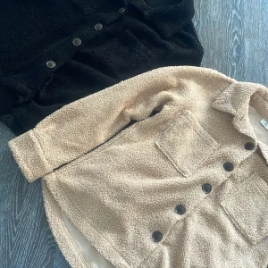 Beige  teddyjacka - En  mysig teddyjacka i beige med knappar framtill. Perfekt för kyligare dagar med sin mjuka och fluffiga textur. Jackan har långa ärmar och en klassisk krage. Köpt från Åhléns, st S/M. 