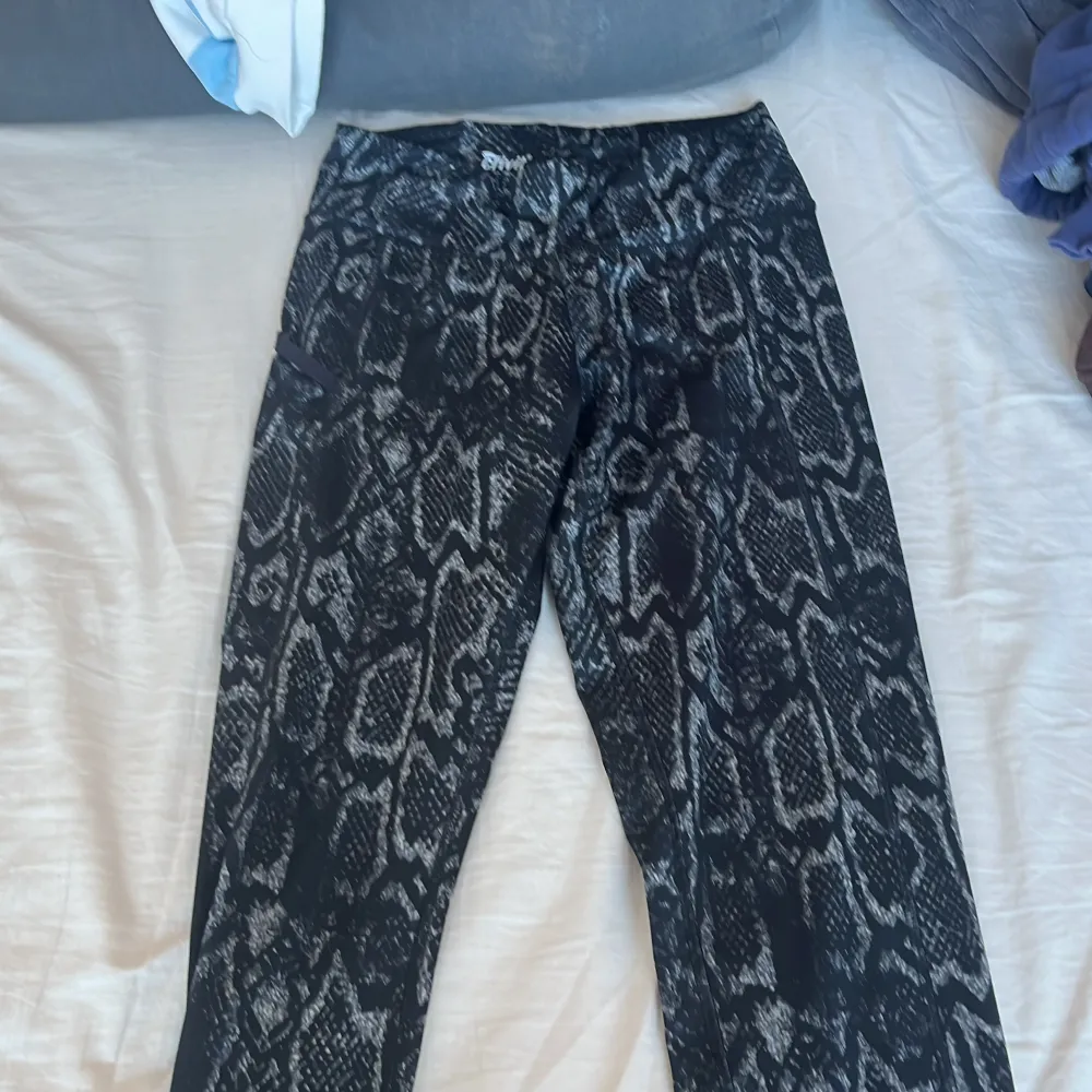 Snygga svarta leggings från Crivit med ett coolt mönster som påminner om ormskinn. Perfekta för en trendig look och bekväma att bära. Passar bra till både träning och vardag.. Farkut & Housut.