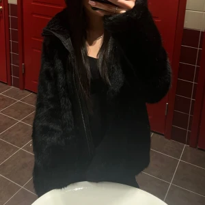 Svart pälsjacka med dragkedja - Säljer en snygg svart pälsjacka med dragkedja. Jackan har en mjuk och fluffig yta som ger en lyxig känsla. Perfekt för att hålla sig varm och stilren under kyliga dagar. Passar till många olika outfits!