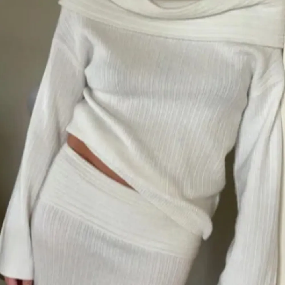Snygg vit ribbad topp med offshoulder-design och långa ärmar. Perfekt för en stilren look. Den har en figurnära passform och är gjord i ett mjukt material. Säljer även matchande kjol. Neuleet.