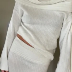 Vit ribbad klänning - Snygg vit ribbad topp med offshoulder-design och långa ärmar. Perfekt för en stilren look. Den har en figurnära passform och är gjord i ett mjukt material. Säljer även matchande kjol