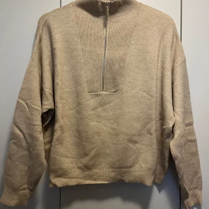 Beige stickad tröja från Stradivarius - Säljer en beige stickad tröja från Stradivarius med dragkedja framtill. Tröjan har en hög krage och långa ärmar. 