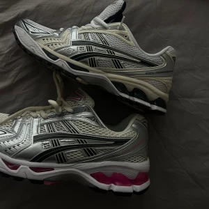 Vita och silverfärgade sneakers från Asics - Snygga sneakers från Asics i vitt och silver med svarta detaljer. Skorna har en sportig design med snörning och en bekväm sula. Perfekta för träning eller en aktiv vardag. Säljer de med rosa. Slut överallt, 