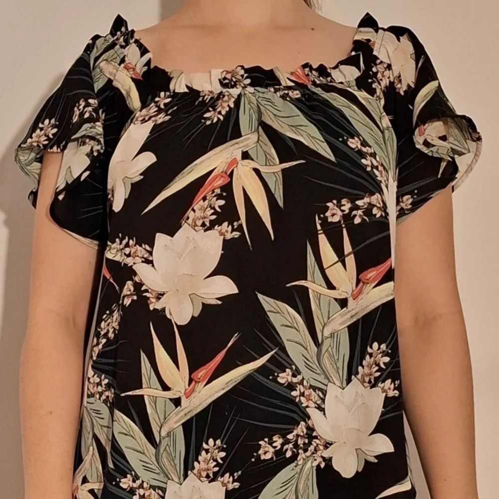 Svart blus med blomstermönster som kan bäras off-shoulder eller 