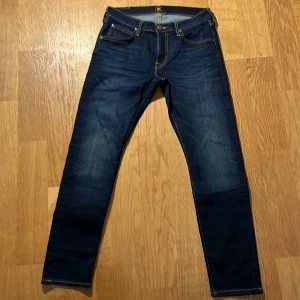 Mörkblå jeans från Lee - Säljer ett par snygga mörkblå jeans från Lee. De har en klassisk femficksdesign och är i en slim passform. Jeansen är tillverkade i ett slitstarkt denimtyg och har en bekväm midwaist. Perfekta för både vardag och fest! Jeansen är helt nya nypris 1300