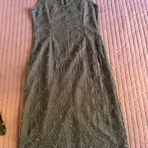 Grå klänning sexiga figursydd ,pärldetaljer från indiska - Säljer en elegant grå klänning från Indiska i storlek S. Klänningen har ett vackert pärlmönster över hela tyget och en stilren v-ringning. Den är ärmlös och har en diskret dragkedja i ryggen. Kläningen ser anarlurlunda Perfekt för festliga tillfäll