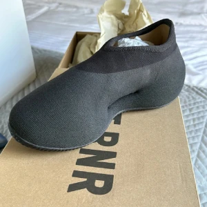 Svarta YZY Knit RNR från Adidas - Säljer ett par svarta YZY Knit RNR från Adidas. De är i nyskick och har en unik, strömlinjeformad design med en tight passform. Perfekta för både vardag och speciella tillfällen. Skorna är gjorda i ett stickat material som ger en modern och stilren look.