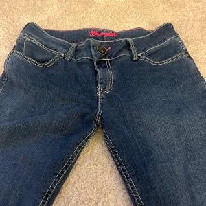 Lågmidjade Jeans - Utsvängda lågmidjade jeans från Wrangler med rosa detaljer i storlek M/38💞Fickorna har broderade detaljer. Köparen står för frakten. Skriv för frågor, mått osv❣️