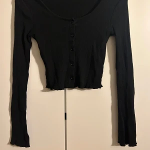 Tunn Svart kardigan  - En tunn svart ribbad kardigan ifrån GinaTricot. Gullig lite vågig detalj vid ärmarna och nere vid tröjans slut. Bra skick! Storlek S men borde även funka på XS.