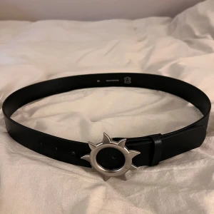 Svart skärp med solformad spänne - Säljer ett svart skärp från Eytys i äkta skinn. Skärpet har ett unikt solformad spänne i silverfärg som verkligen sticker ut. Tillverkat i Portugal och i mycket bra skick. Endast använt ett fåtal gånger men är tyvärr lite slitet pga spännet som slite