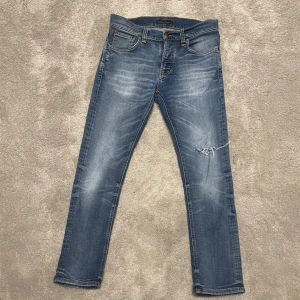 Nudie jeans Grim Tim - Snygga blåa Nudie jeans i modellen Grim Tim. Storlek 30/30. Slitningen på vänsterbenet är design. Fraktar direkt efter köp på köparens bekostnad. Säljs då dem inte passar mig längre. 
