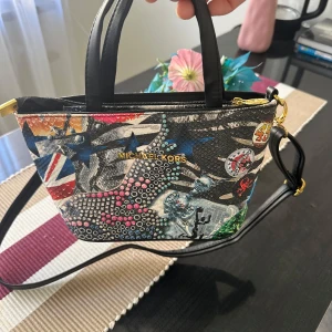 Färgglad axelväska från Michael Kors - Säljer en supercool och färgglad axelväska från Michael Kors. Väskan har ett unikt mönster med olika färger och detaljer, perfekt för att liva upp vilken outfit som helst. Den har en dragkedja upptill och en justerbar axelrem. Perfekt för både vardag och fest!