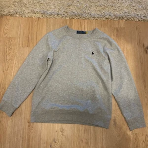 Grå tröja från Polo Ralph Lauren - Säljer en stilren och bekväm grå tröja från Polo Ralph Lauren. Den har en klassisk design med långärmade ärmar och det ikoniska logotypbroderiet på bröstet. Perfekt för både vardag och avslappnade tillfällen. Tröjan är i bra skick och redo för en ny ägare!