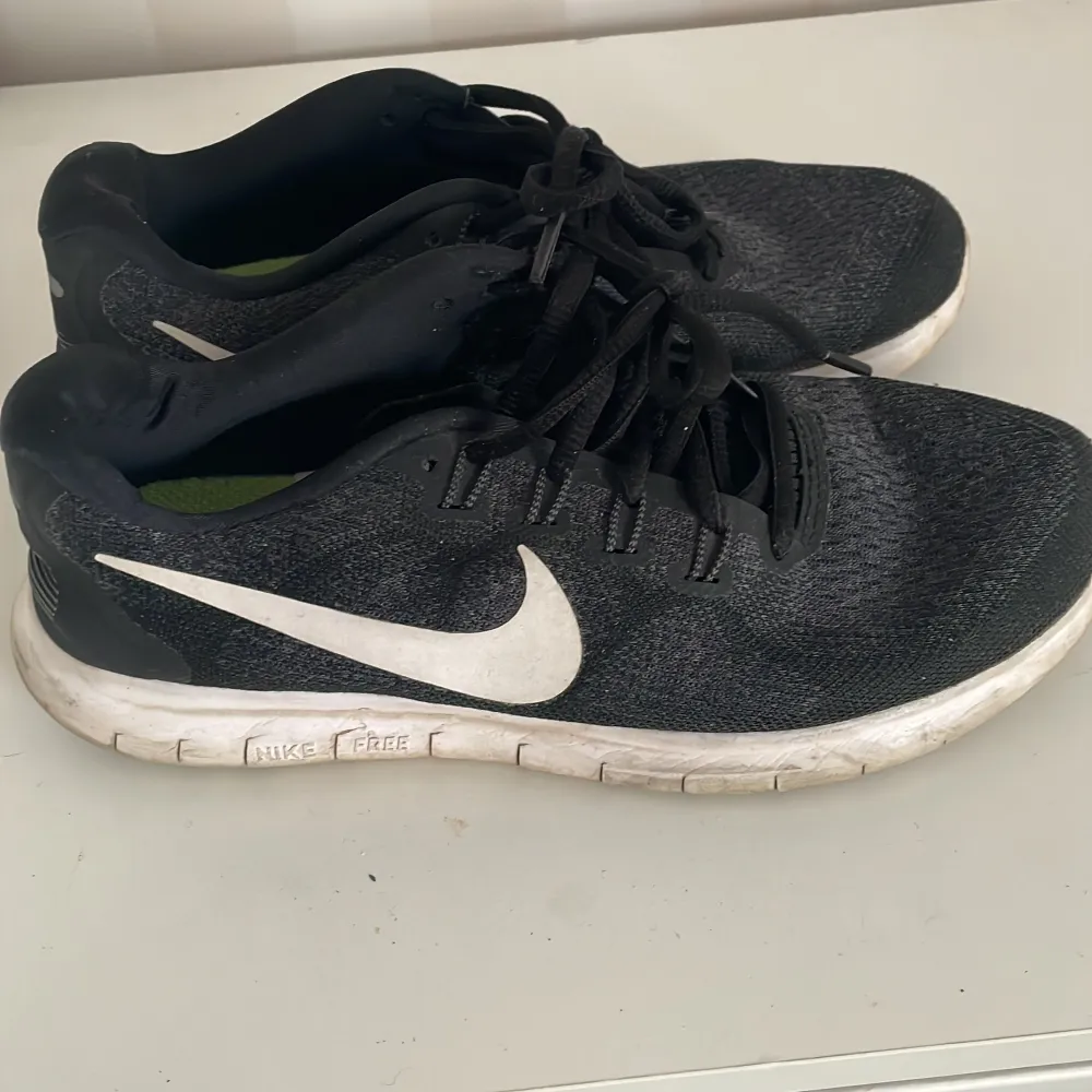 Säljer ett par svarta Nike sneakers i välanvänt skick. De har en vit sula och den klassiska Nike-loggan på sidan. Skorna har snörning och är perfekta för träning eller vardagsbruk. Insidan är grön vilket ger en cool kontrast. Passar bra för dig som gillar en sportig stil.. Skor.