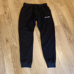 Svarta mjukisbyxor från Champion - Säljer ett par svarta mjukisbyxor från Champion. De har en bekväm passform med resår och snörning i midjan. Perfekta för en avslappnad dag hemma eller lätt träning. Byxorna har en liten Champion-logga på framsidan och baksidan. De är i ny skick knappt använda. Köpta för 750kr