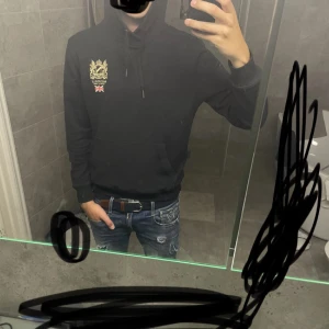 Svart hoodie från Morris - Säljer en snygg svart hoodie från Morris i storlek S. Den har en broderad logga och brittisk flagga på bröstet. Perfekt för höst och vinter med sin mysiga känsla. Den har en klassisk känguruficka och justerbar huva. Passar både till vardags och chillkvällar. 