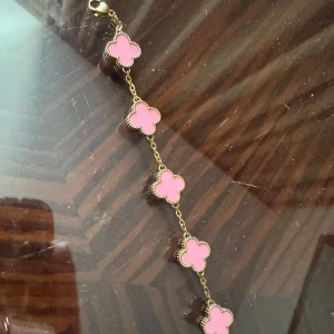 Guldarmband med rosa blommor - Säljer ett superfint guldarmband med små rosa blommor. Perfekt för att ge en färgklick till din outfit! Armbandet har en tunn kedja och blommorna är jämnt fördelade längs med den. Passar både till vardags och fest. 🌸