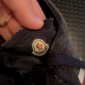 Mörklblåa sneakers från Moncler - Säljer ett par snygga mörkblåa sneakers från Moncler i mocka. De har en cool röd och vit randdetalj på sidan och klassisk snörning. Perfekta för både vardag och fest! Skorna är i bra skick och Är i storlek 42! 