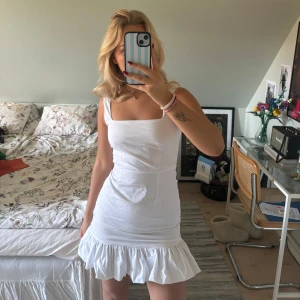 Vit kortklänning med volangdetalj🤍 - Säljer en superfin vit kortklänning med volangdetalj längst ner. Klänningen är ärmlös och har en tight passform. Perfekt till studenten eller en fin sommardag🤍 Med tillhörande band som man kan knyta runt ärmarna. 