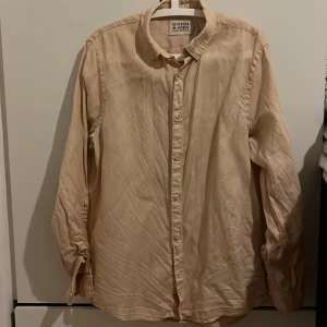 Linne skjorta från Scotch & Soda - Säljer en snygg beige skjorta från Scotch & Soda i storlek M - Regular fit. Många fina detaljer. Skjortan är långärmad och har en klassisk krage med knappar hela vägen ner. Den är i 100% linne och har en broderad logga på sidan. Unik färg med några orange detaljerade broderier