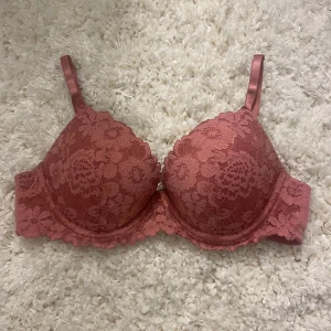 Rosa spets-bh - Säljer en superfin rosa bh med spetsdetaljer. Den har justerbara axelband och en klassisk hakknäppning bak. Använd ett fåtal gånger, så den är i bra skick. Den har lite pushup!