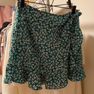 Grön kjol storlek 38 - Kjol med blommönster och en volang, aldrig använd!