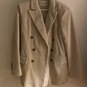 Kavaj från NA-KD - 🌹 Fin beige/grå kavaj i manchesterliknande tyg och med axelvaddar från NA-KD 🌹 Storlek 34 men stor i storleken 🌹Passar som kavaj nu på vintern och som jacka på våren 🌹 Knappt använd så i fint skick